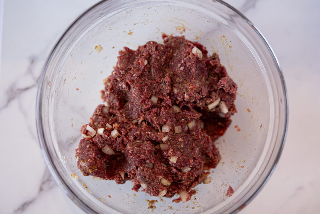 Ground meat mixed with other ingredients in a glass bowl