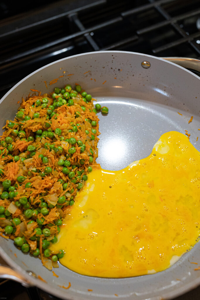 Peas and shredded carrots cooked in a pan with beaten eggs in it