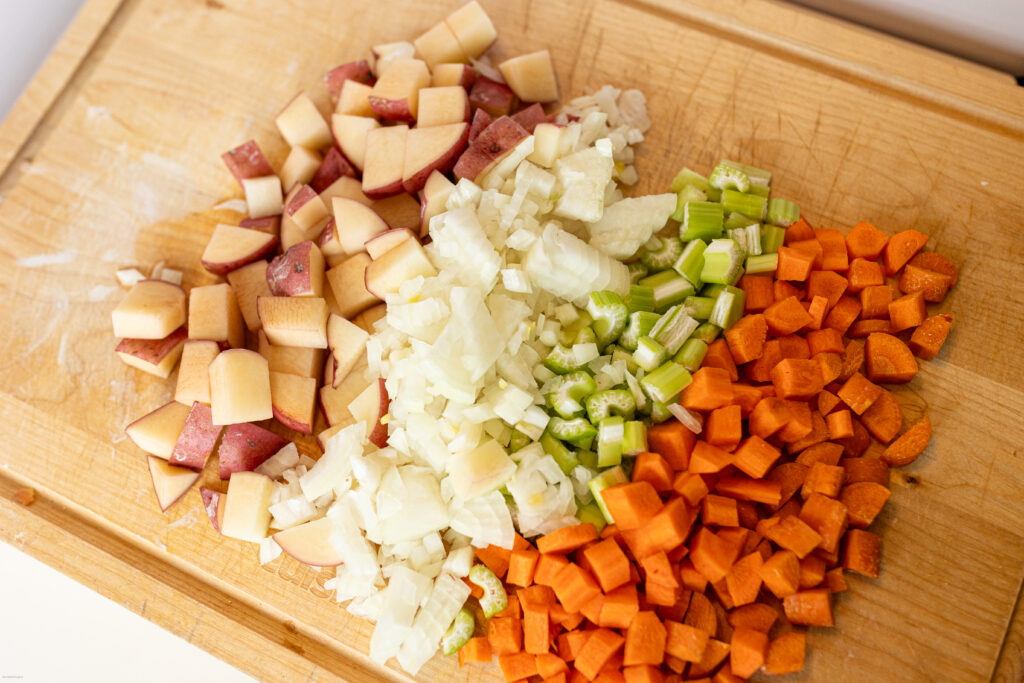 Potatoes, onion, celery, carrots all cut up on a cutting board